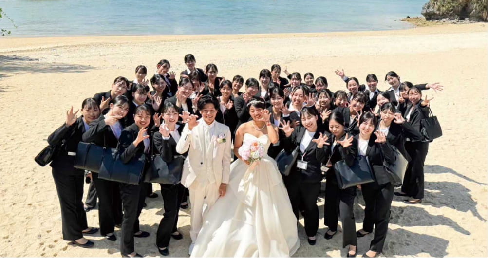 海辺で新郎新婦を囲んで写真を撮る大勢のスタッフ